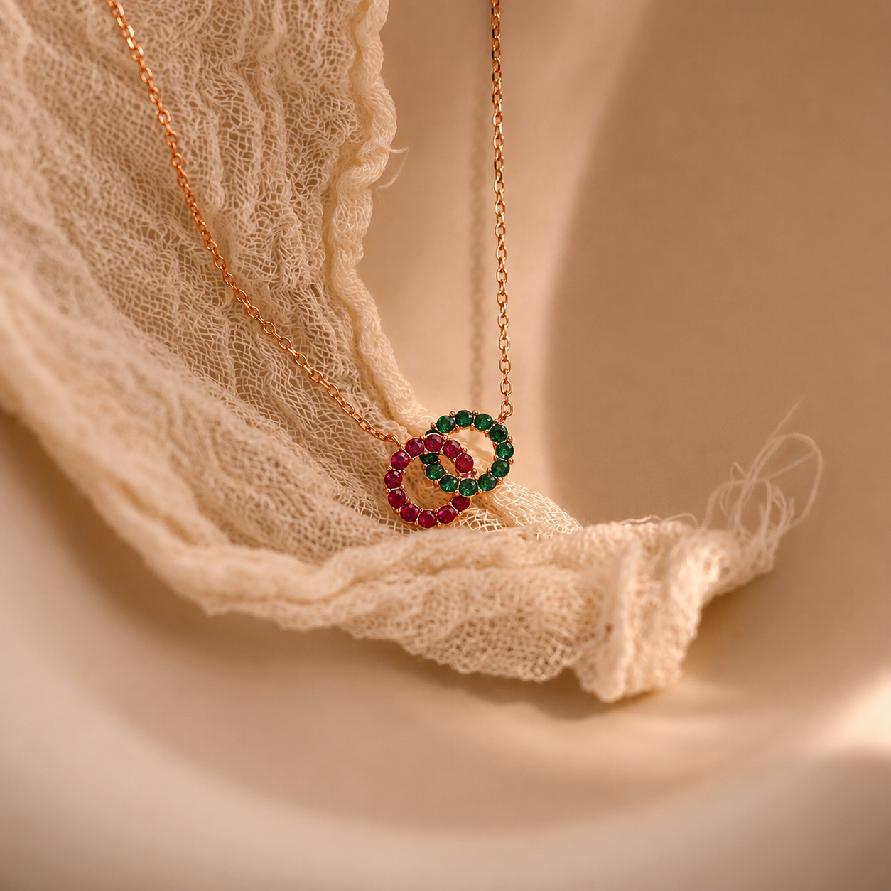 Necklace with a heart-shaped pendant featuring red and green gemstones on a soft fabric background.